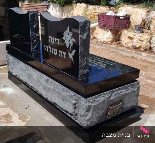 מצבה שחורה עם כיתוב ופרח חקוק